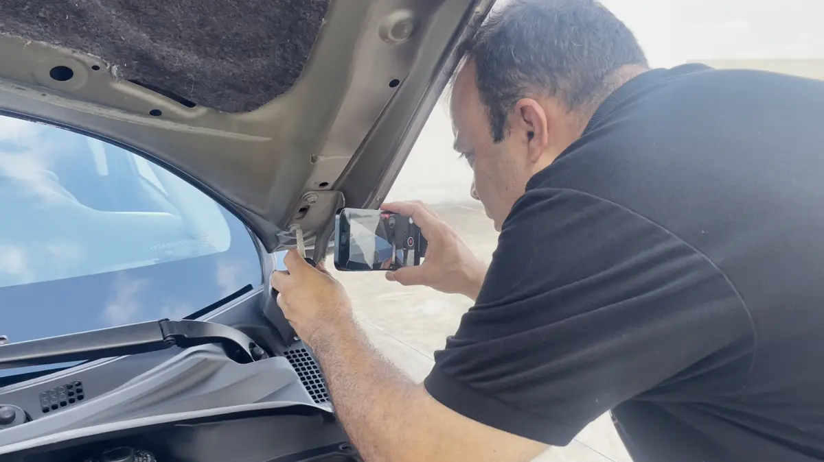 Edson fotografa a dobradiça do capô de um carro