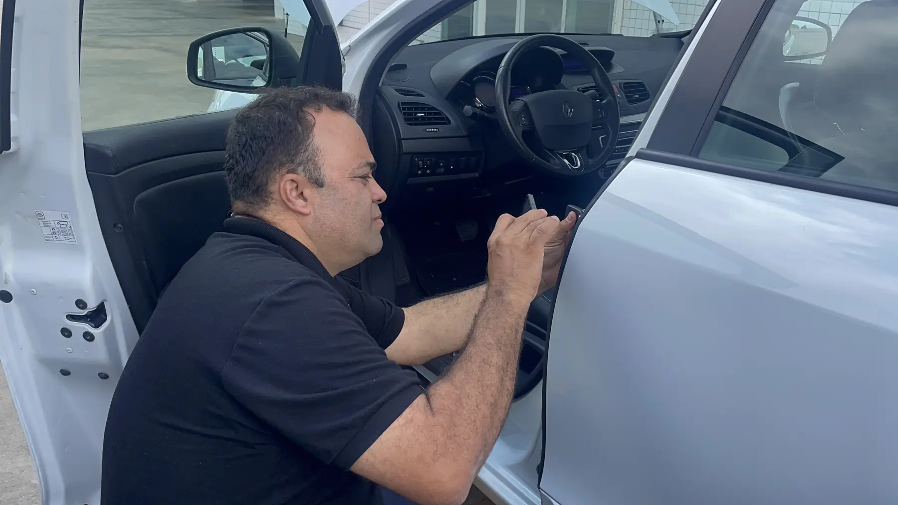 Edson Viana agachado ao lado de um carro, examinando a coluna da porta